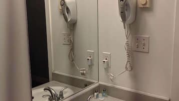 A bathroom with a sink, a mirror, and two hair dryers mounted on the wall.