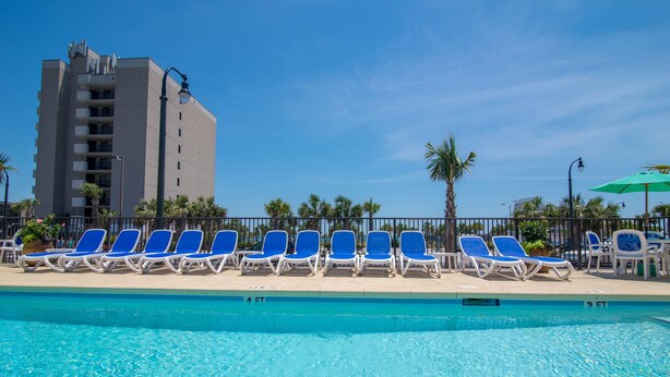 A swimming pool with blue lounge chairs and a tall building in the background. - The Darlington Cottages (Myrtle Beach)
