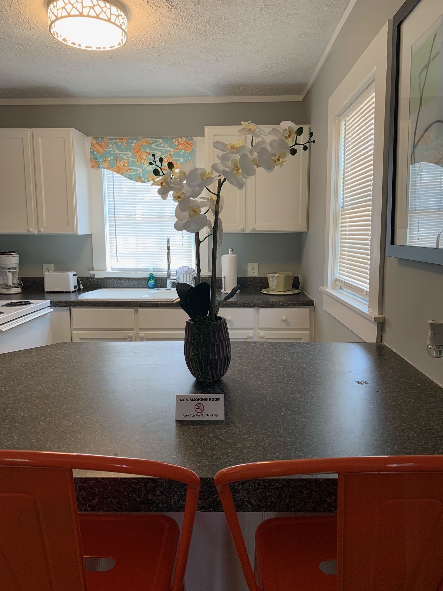 A kitchen with white cabinets, a granite countertop, a vase with white orchids, and a 'Non-Smoking Room' sign.