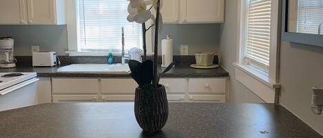 A kitchen with white cabinets, a granite countertop, a vase with white orchids, and a 'Non-Smoking Room' sign.