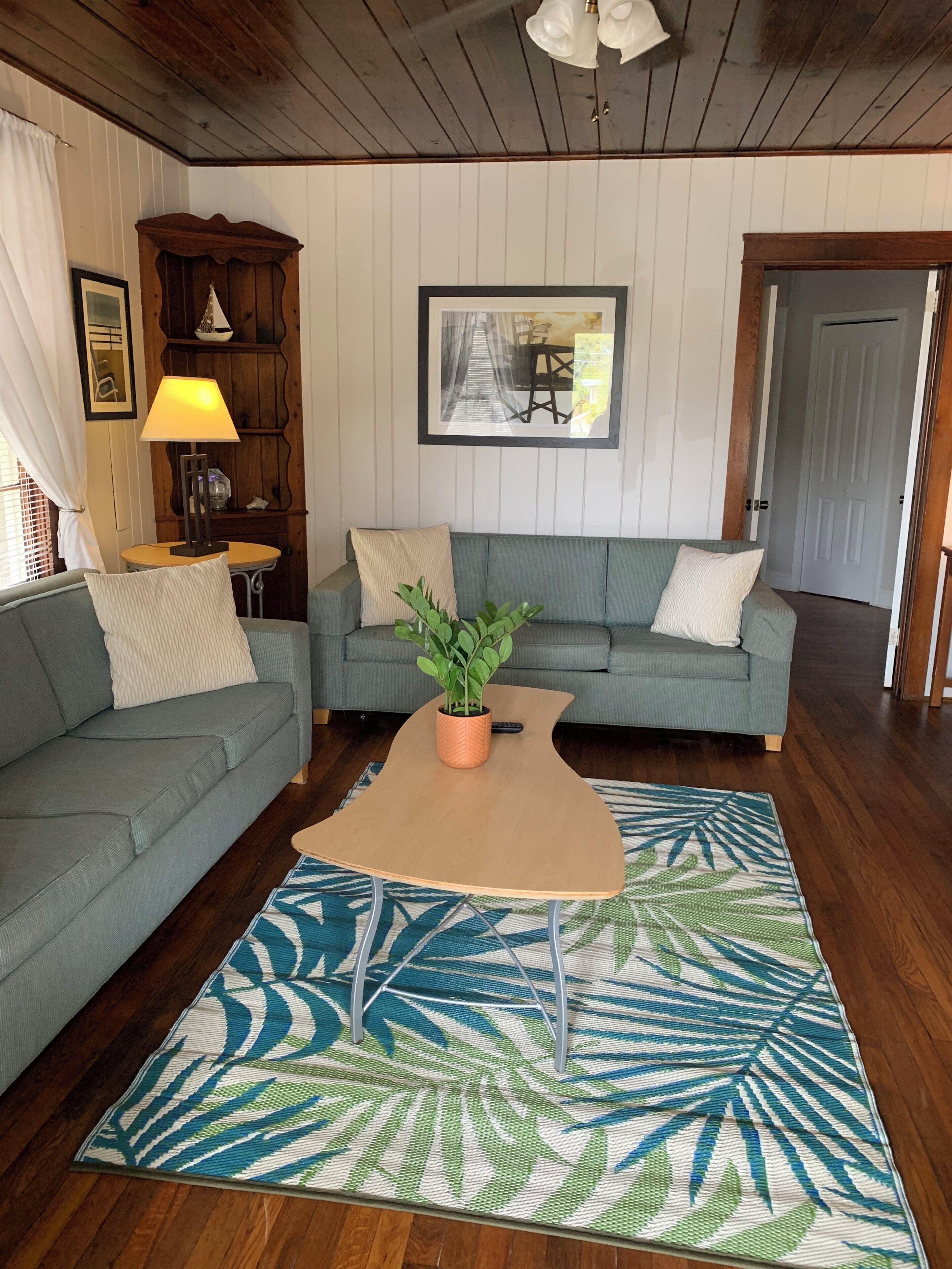 A living room with a sofa, a coffee table, a plant, a lamp, a picture frame, and a door.