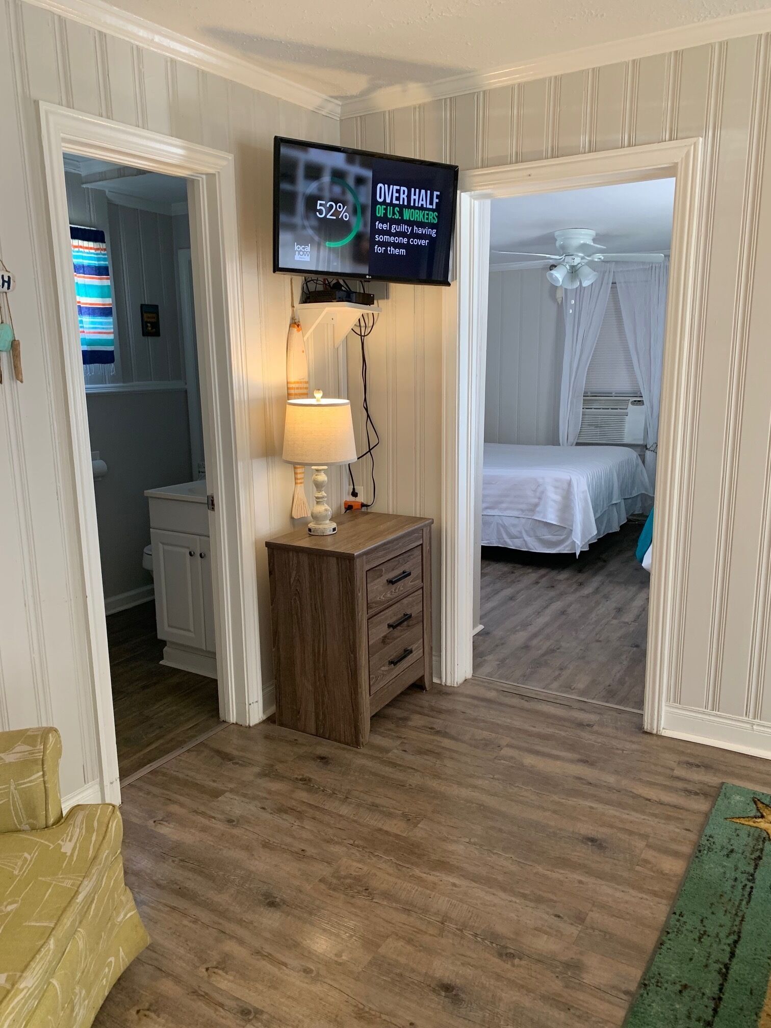 Une chambre d’hôtel avec une commode en bois, une lampe, un téléviseur affichant des statistiques et un lit à baldaquin.