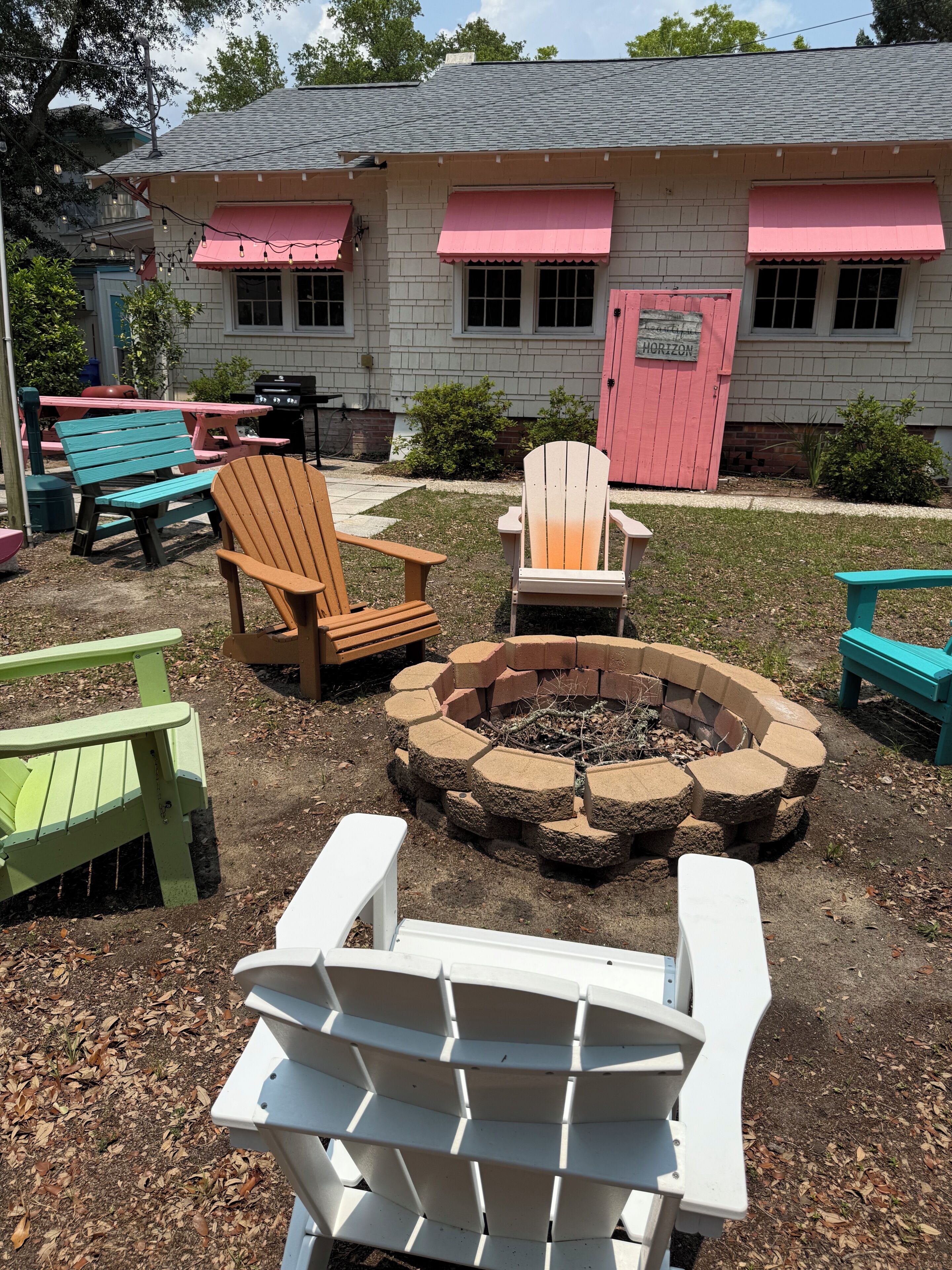 Un jardin avec des fauteuils Adirondack, un foyer extérieur et une maison dotée d’auvents roses.