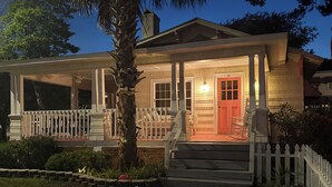 A two-story house with a porch, a red door, and a white picket fence. - The Darlington Cottages (Myrtle Beach)