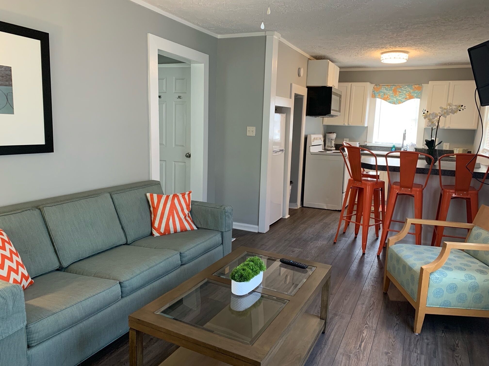 A living room with a sofa, coffee table, and chairs. There is a kitchen area with a refrigerator, microwave, and bar stools.