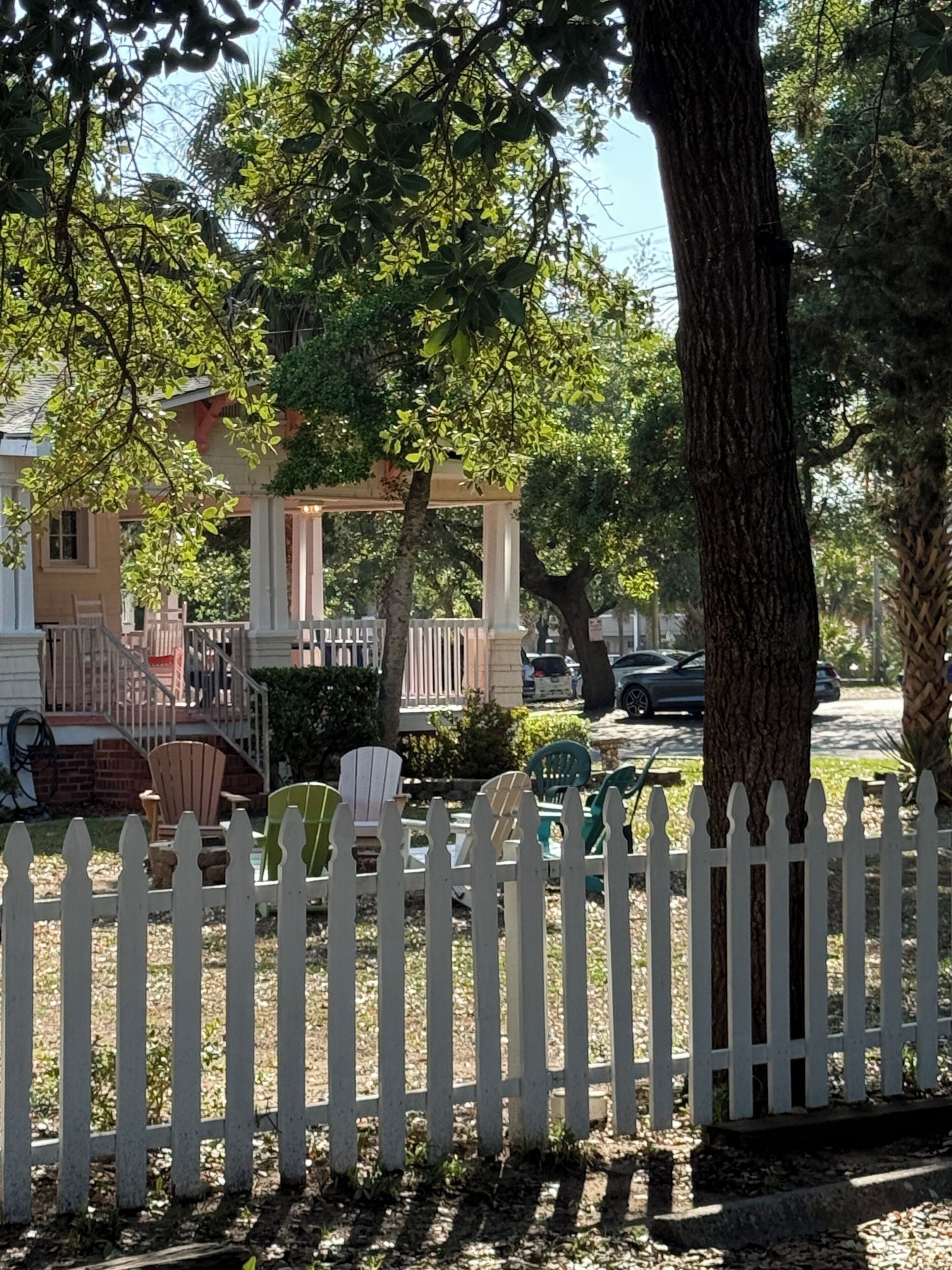 A residential area with a white picket fence, a porch, and a tree.