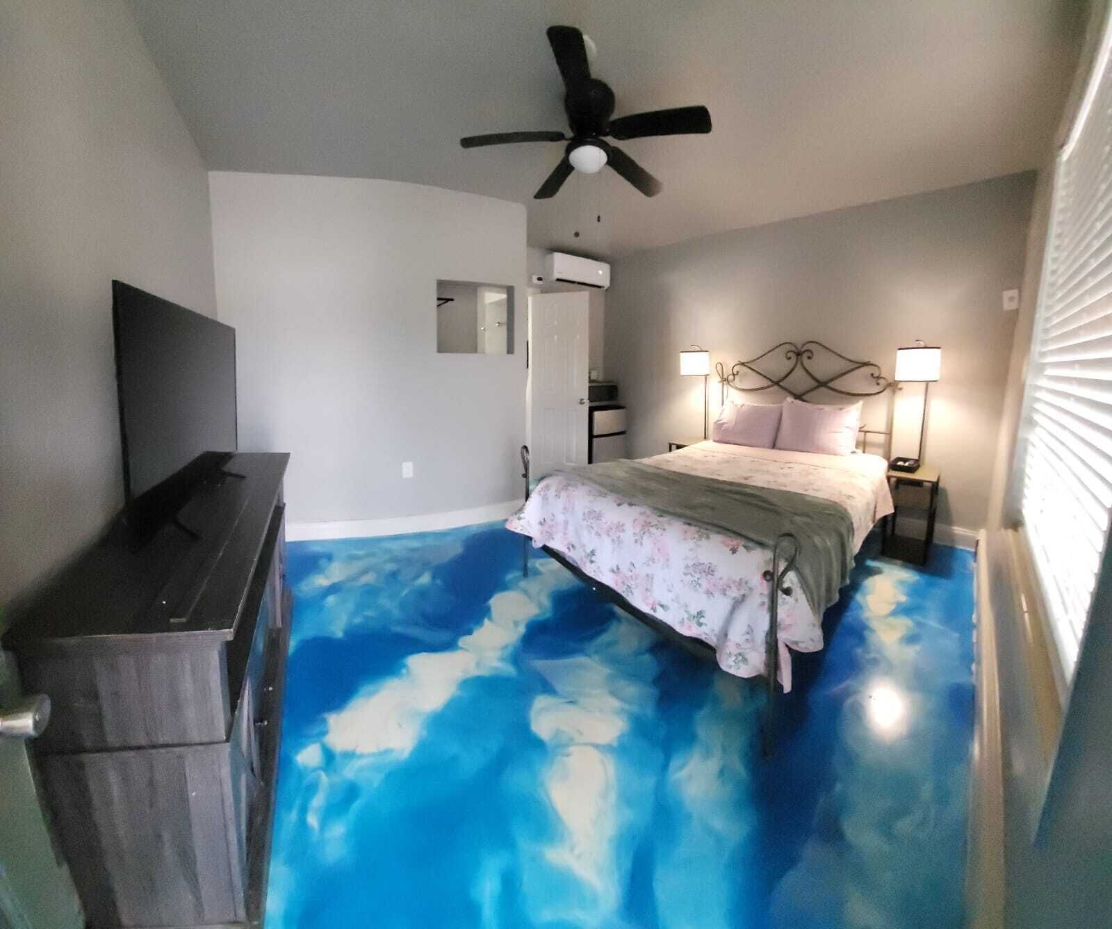 A bedroom with a bed, a ceiling fan, a TV, and a bathroom door.