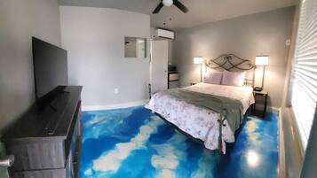 A bedroom with a bed, a ceiling fan, a TV, and a bathroom door.
