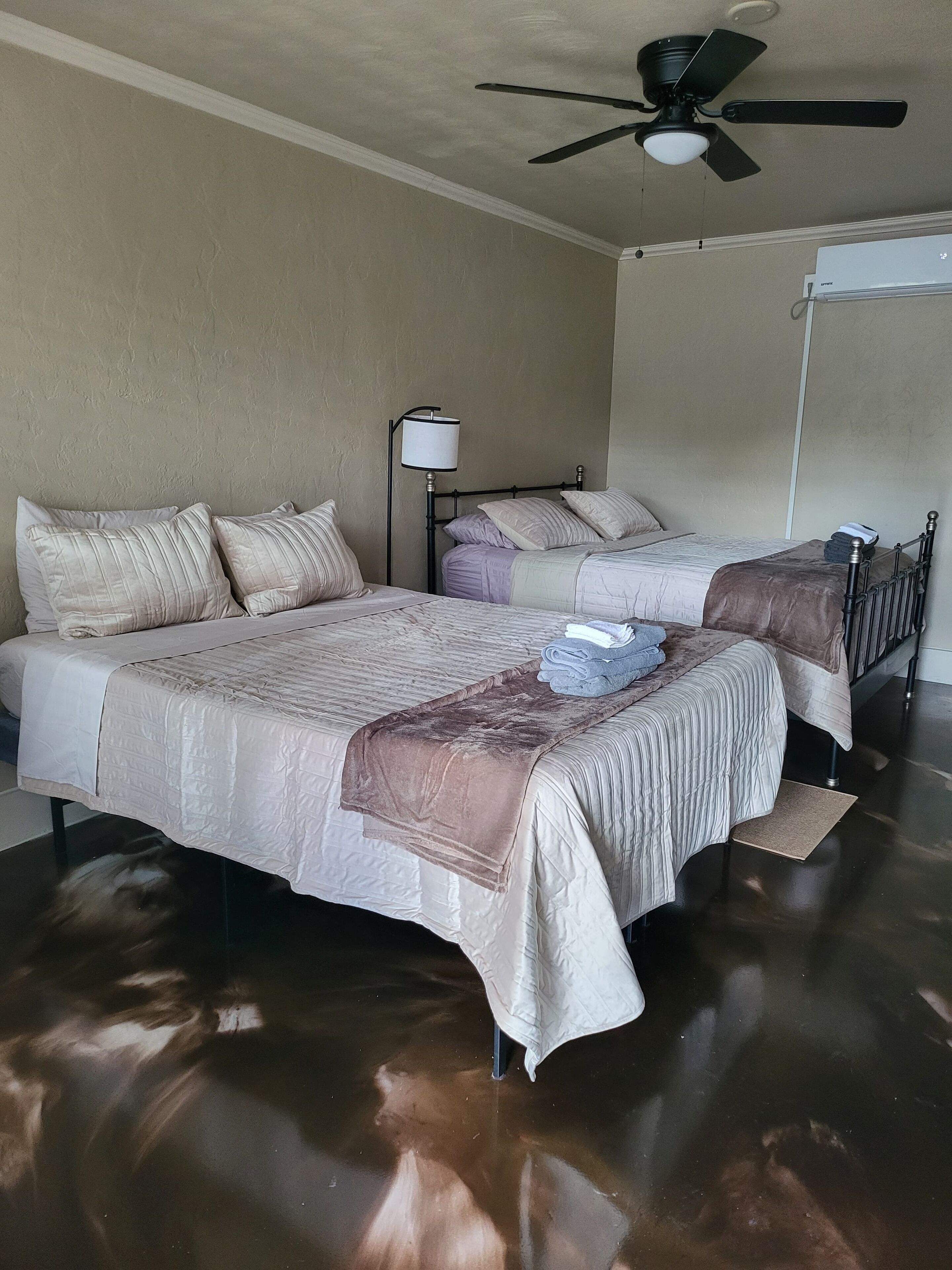 A hotel room with two beds, a ceiling fan, a lamp, and a whiteboard on the wall.