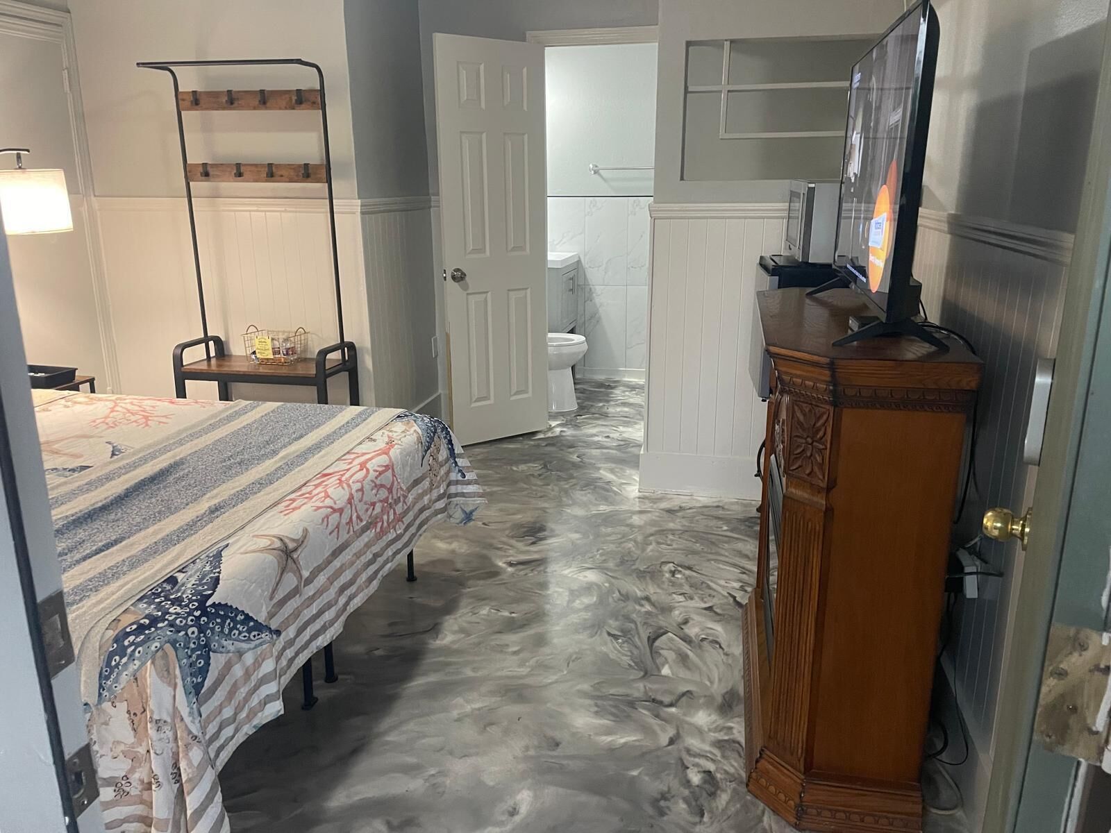 A bedroom with a bed, a dresser, a mirror, and a door leading to a bathroom.