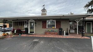 A building with a brick facade, a small tower with a weather vane, and a covered entrance area. - Shamrock Cove Inn (Ocala)