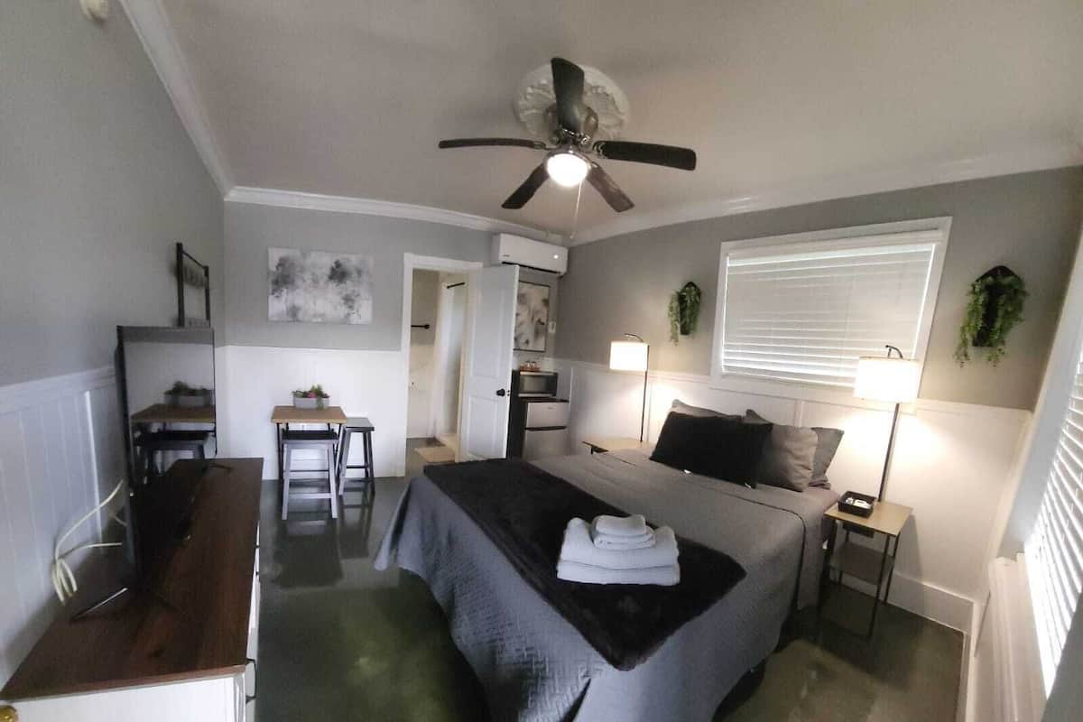 Una habitación compacta con cama, mesitas de noche, un escritorio y un ventilador de techo.
