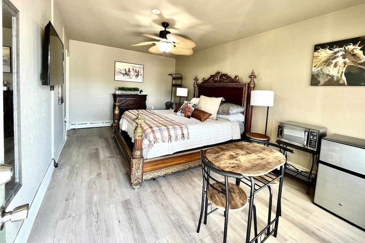 Un dormitorio con cama, ventilador de techo, mesita de noche, lámpara, microondas y refrigerador.
