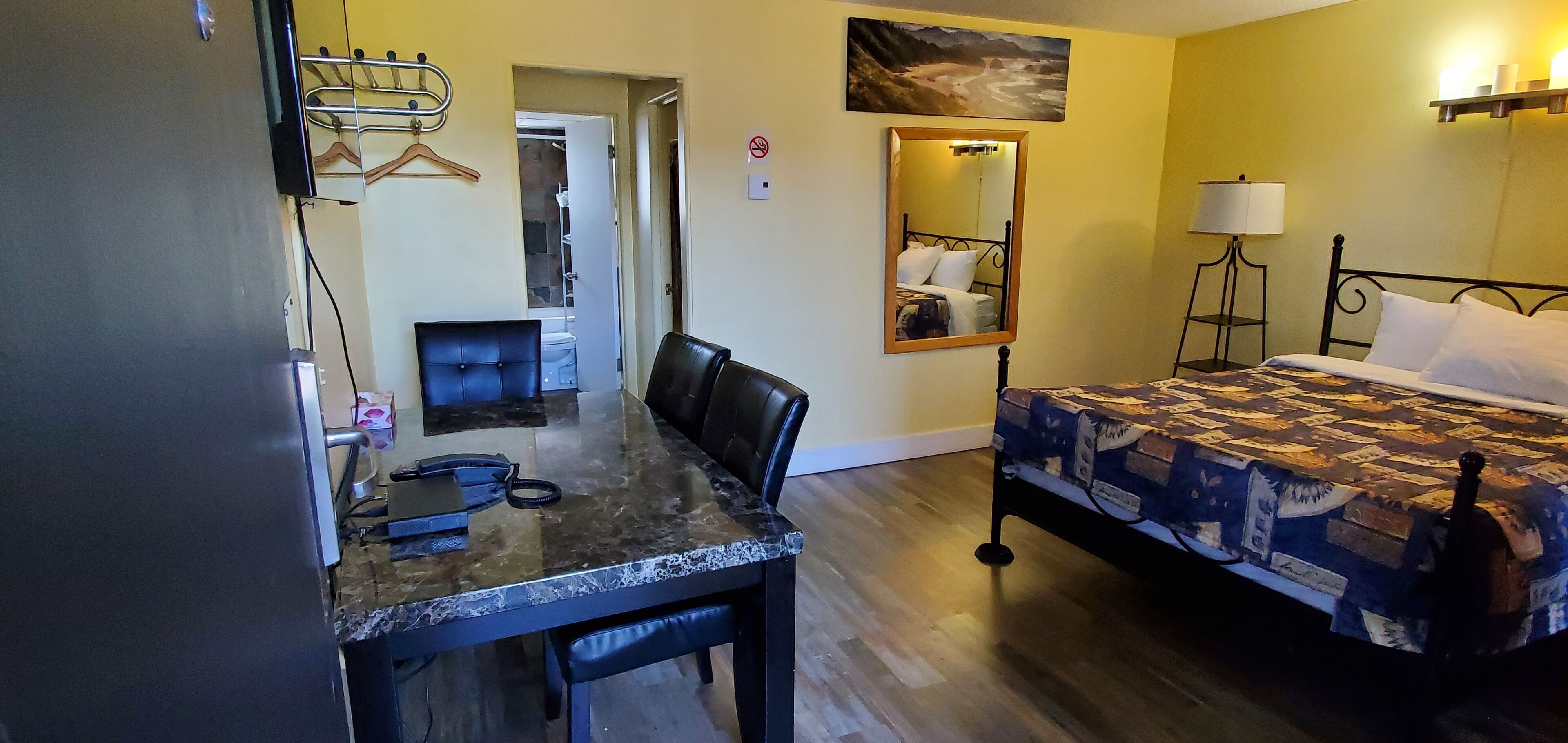 Habitación de hotel con cama, escritorio con silla, espejo y perchero.