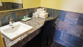 Un bagno con lavandino bianco, piano di lavoro in marmo e asciugamani impilati a parete.