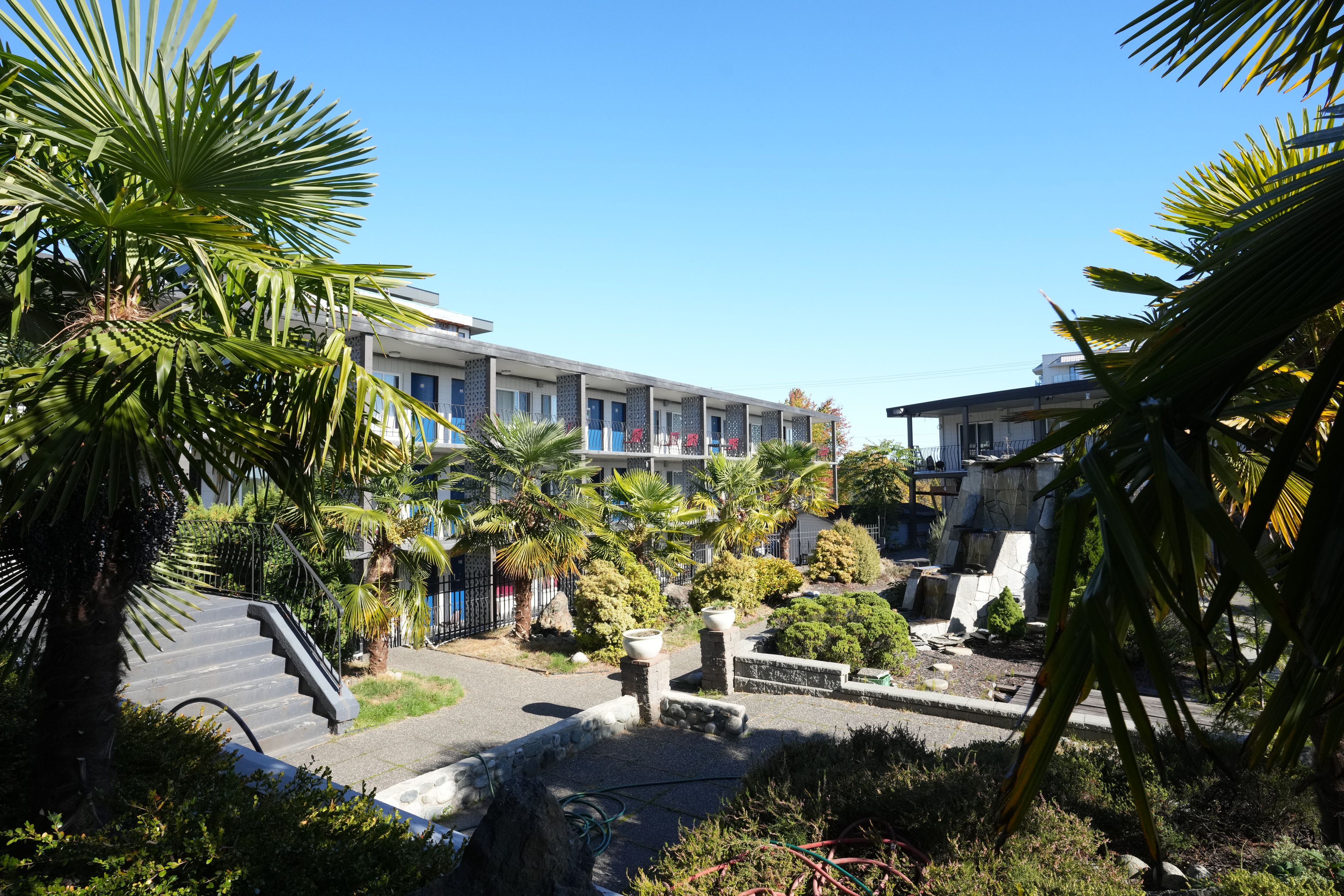 A hotel courtyard with a central fountain, palm trees, and a staircase leading to the building.