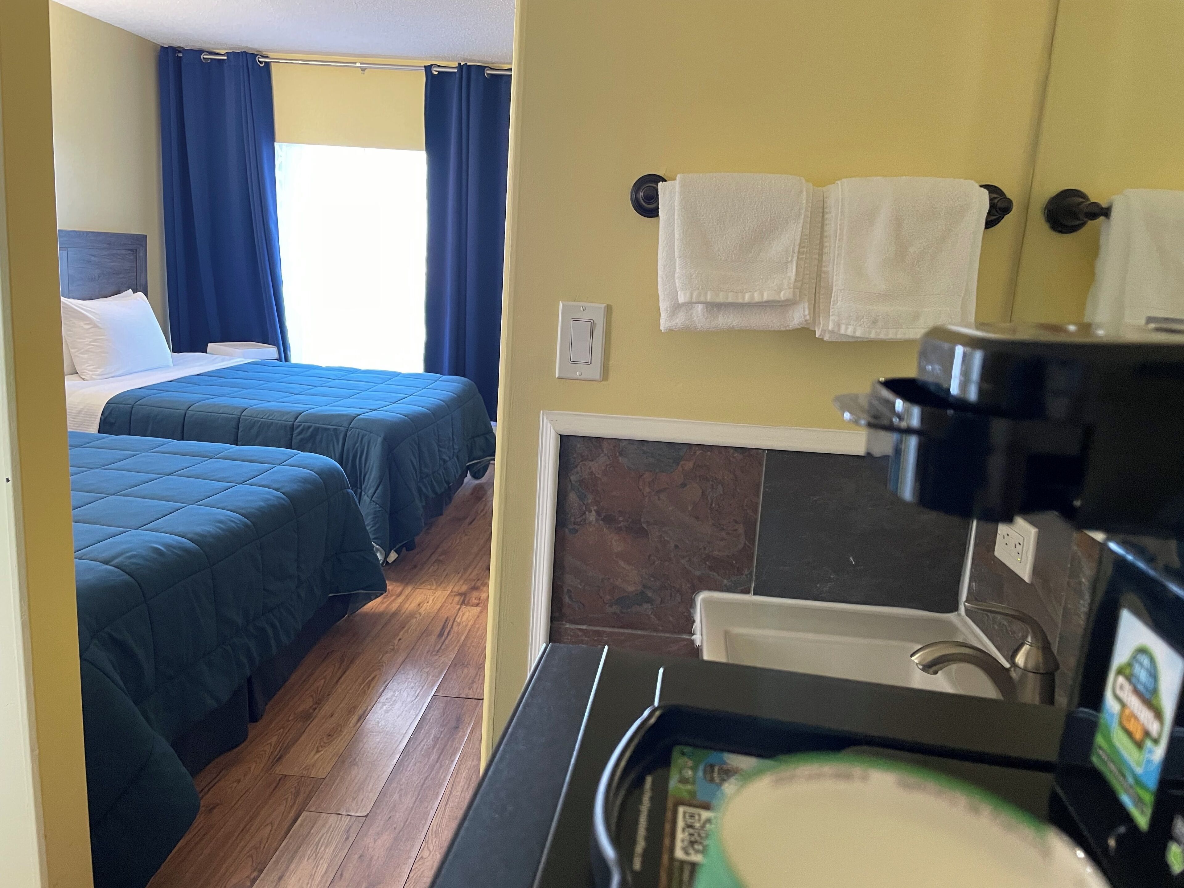 Una habitación de hotel con dos camas, un baño con lavamanos y una cafetera.