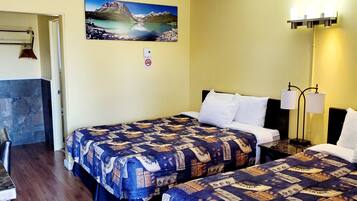 A hotel room with two beds, a painting of a mountain lake, a no-smoking sign, and a lamp.