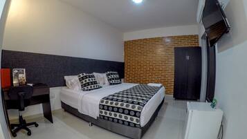A hotel room with a bed, a desk, a chair, a TV, and a small white appliance.