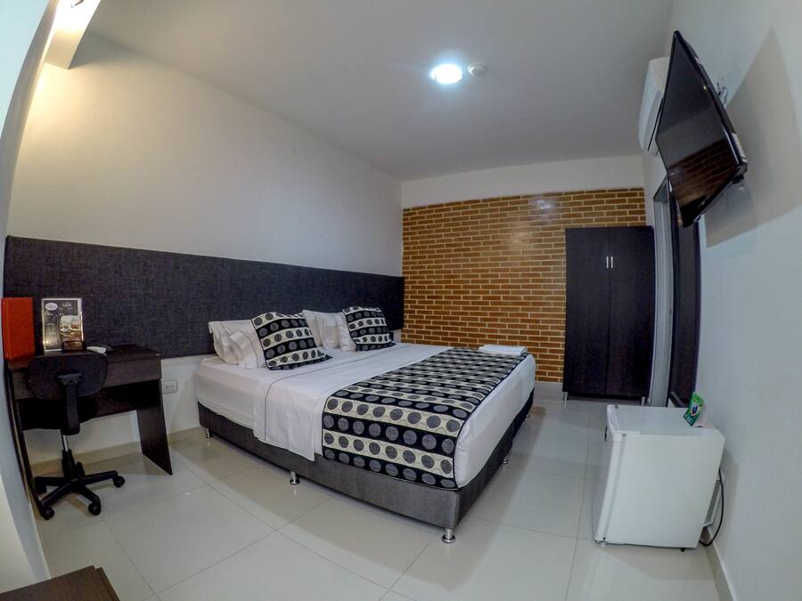 A hotel room with a bed, a desk, a chair, a TV, and a small white appliance.