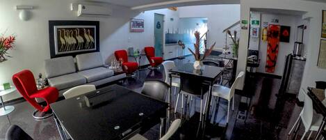 A modern living room with a black dining table, red and white chairs, a grey sofa, and a kitchen area in the background.