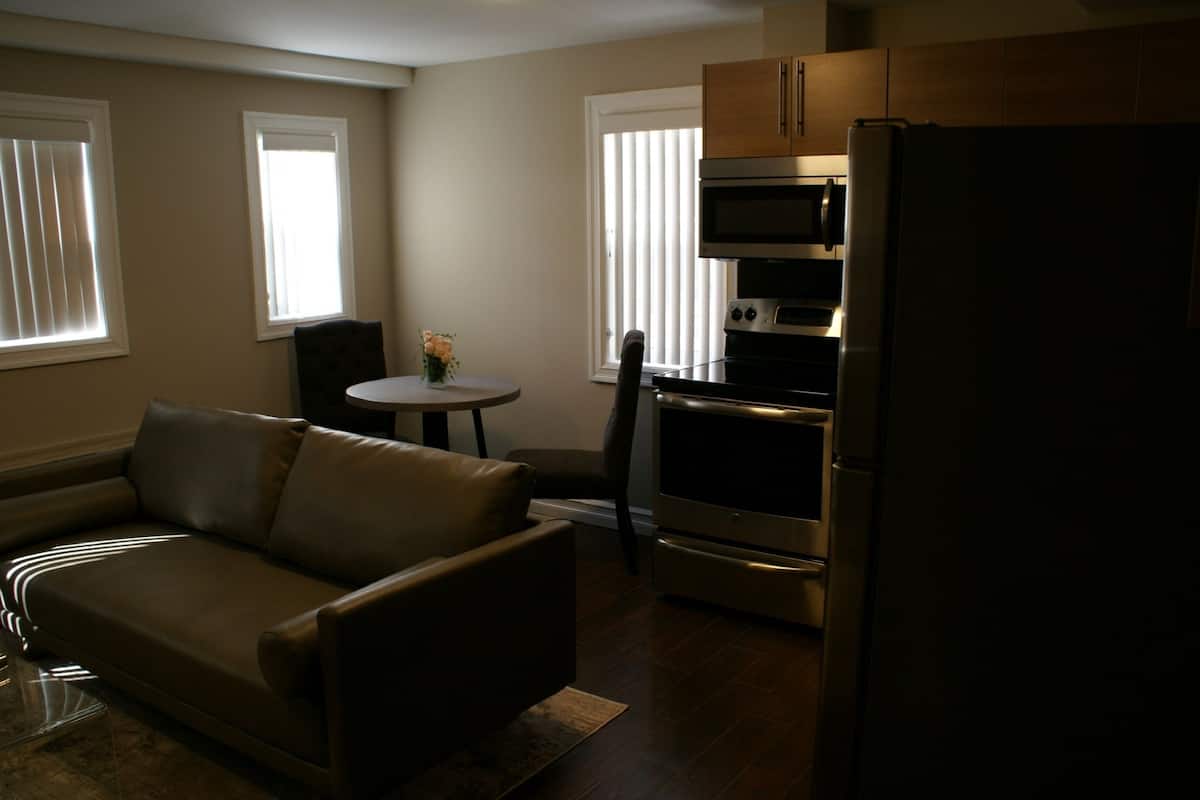 A living room with a sofa, a small table with flowers, and a kitchen area with a refrigerator, oven, and microwave.