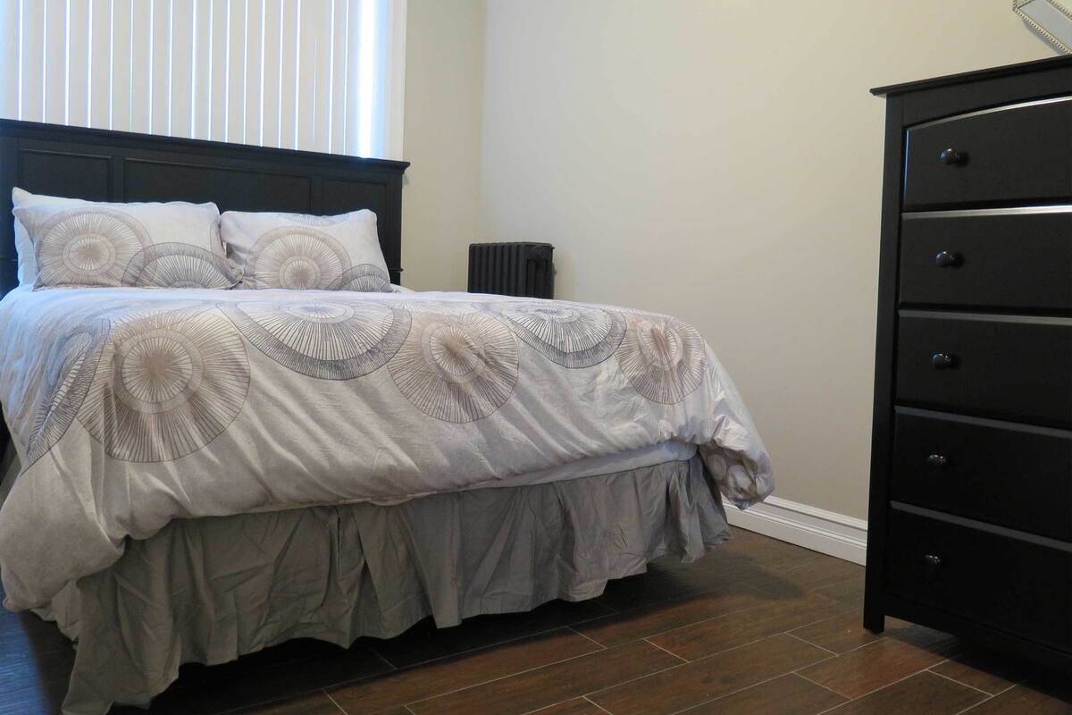 A bedroom with a bed, a dresser, and a radiator.