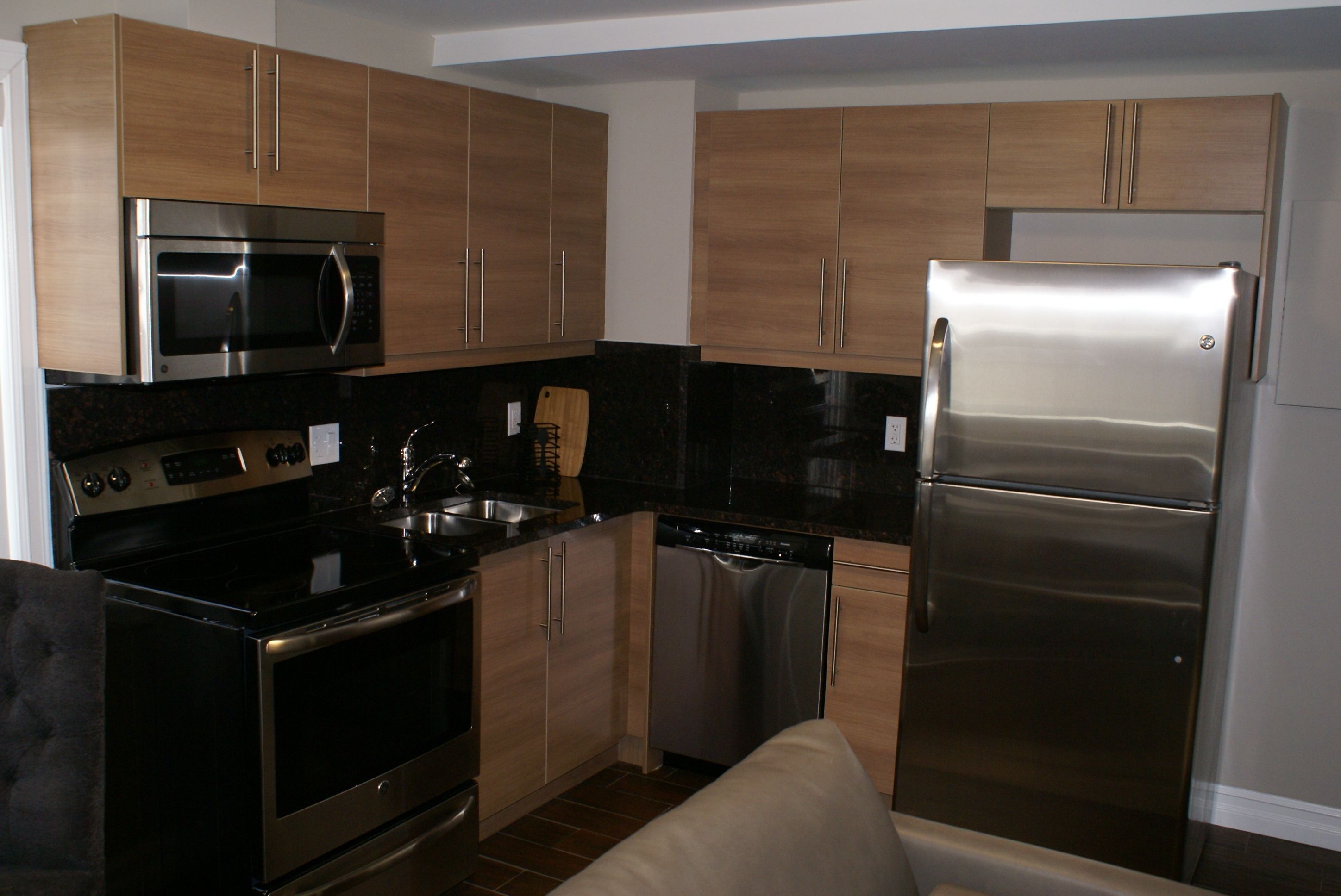 A modern kitchen with stainless steel appliances, wooden cabinets, and a black countertop.