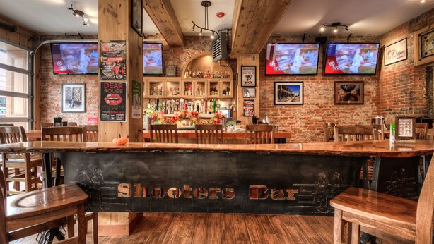 A bar with wooden furniture and brick walls, featuring multiple TVs and a sign reading "Shooters Bar". - Western Hotel & Executive Suites (Guelph)