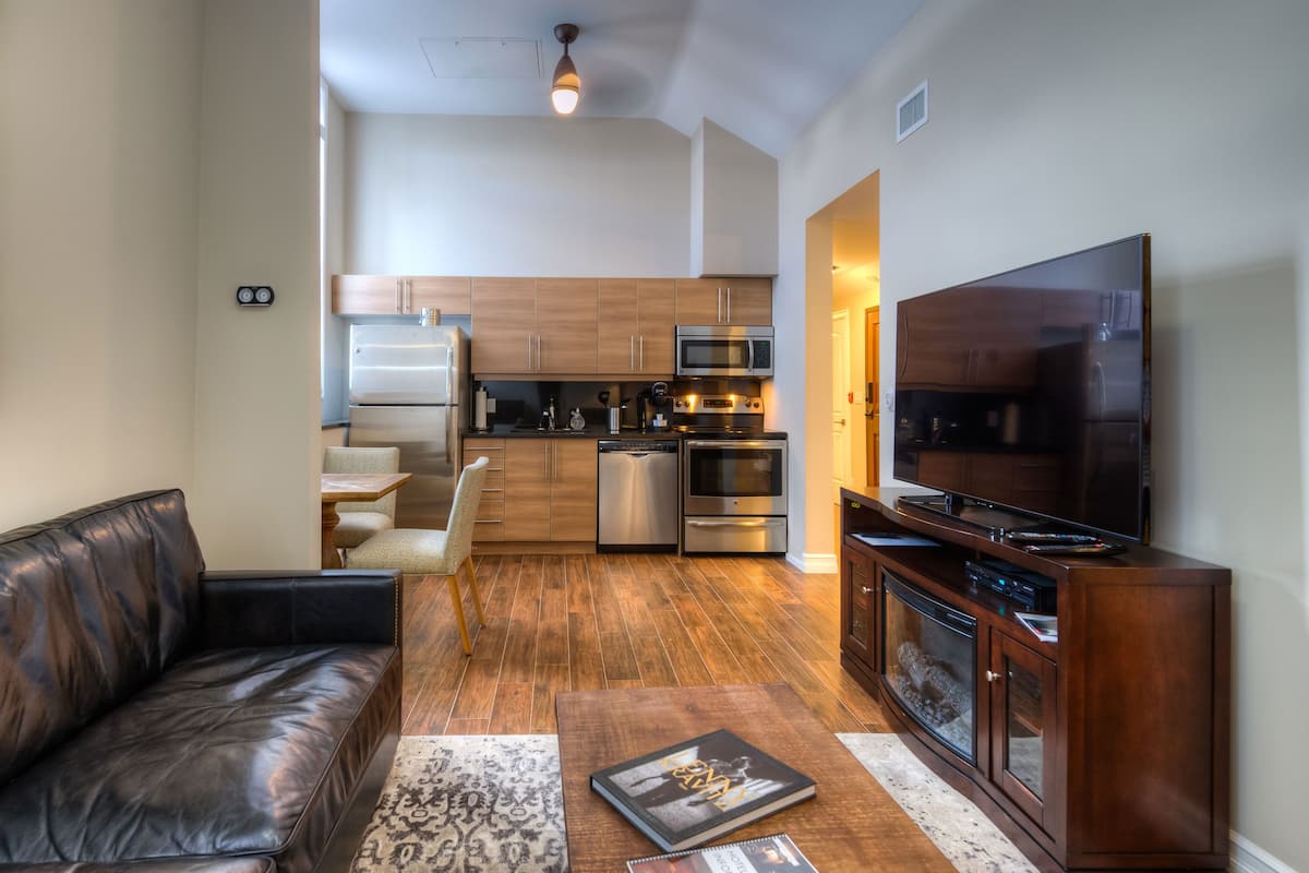 A modern kitchen with stainless steel appliances, a dining area with a leather couch, and a flat-screen TV.
