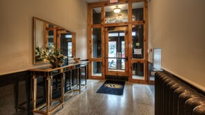 A hallway with a wooden door, a mirror, a console table with a vase, and a radiator. - Western Hotel & Executive Suites (Guelph)