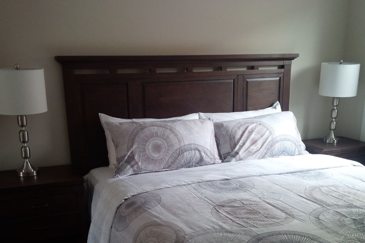 A neatly made bed with a patterned bedspread, a wooden headboard, and two bedside lamps on dark wooden nightstands.