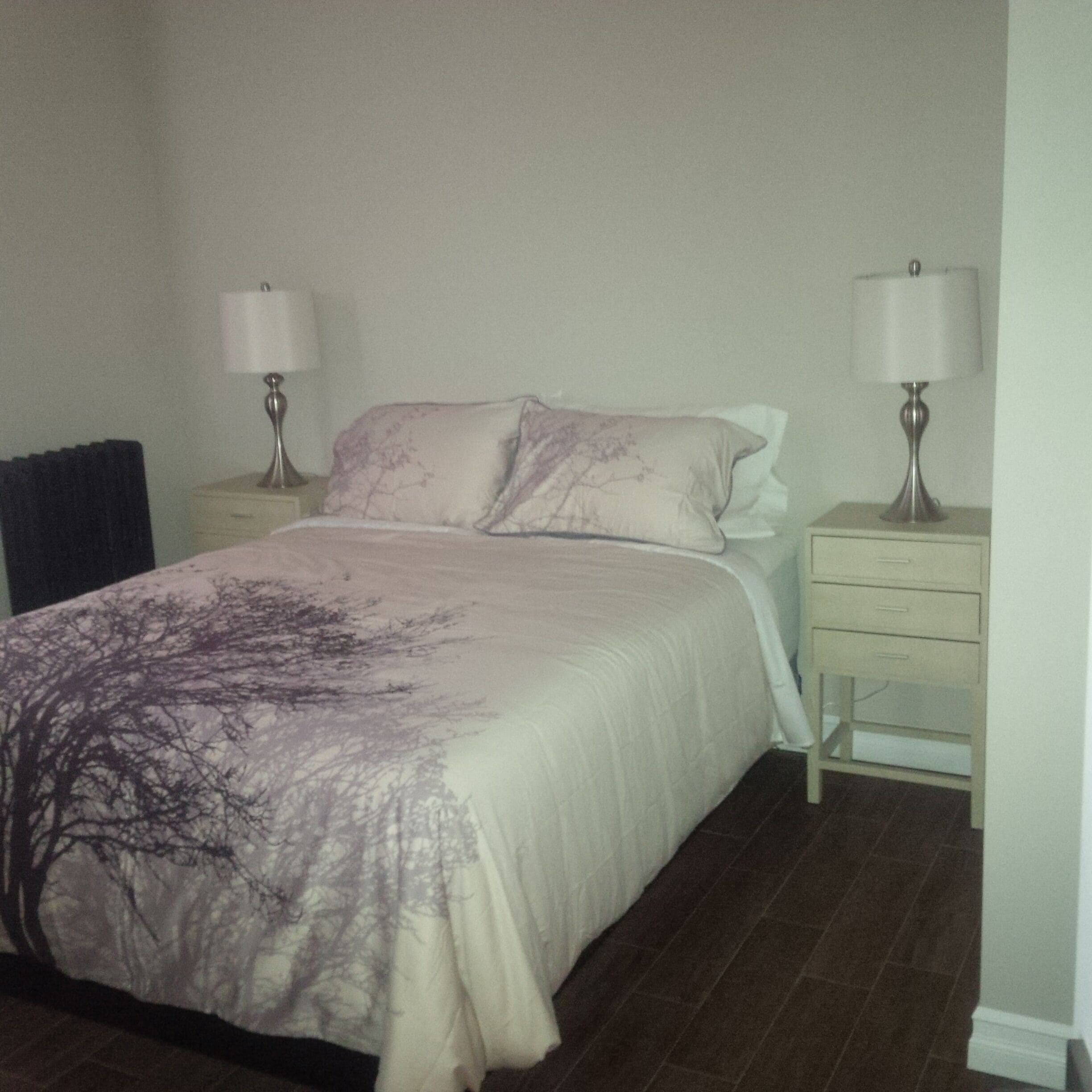A bedroom with a bed, two bedside tables with lamps, a nightstand, and a dresser.