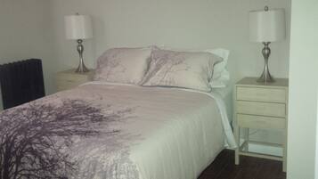 A bedroom with a bed, two bedside tables with lamps, a nightstand, and a dresser.