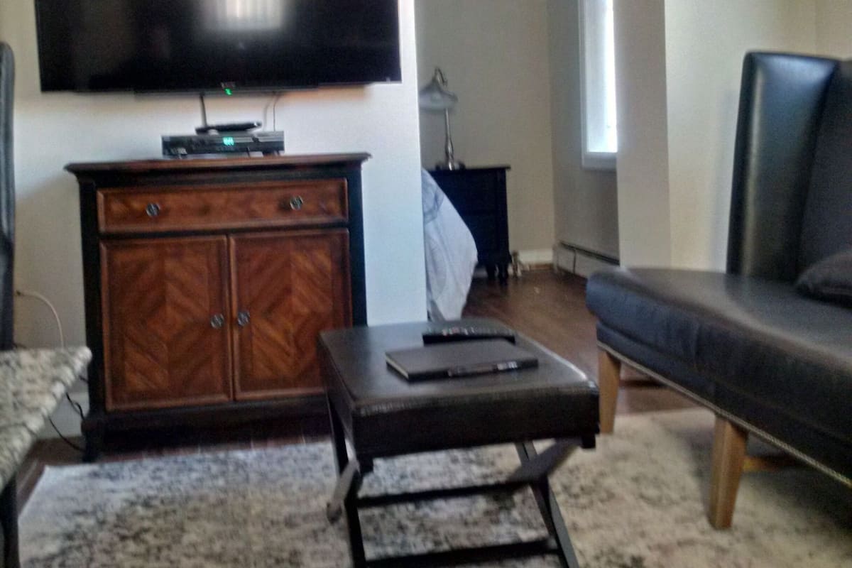 A living room with a flat-screen TV mounted on the wall, a wooden cabinet, a small table, and a sofa.