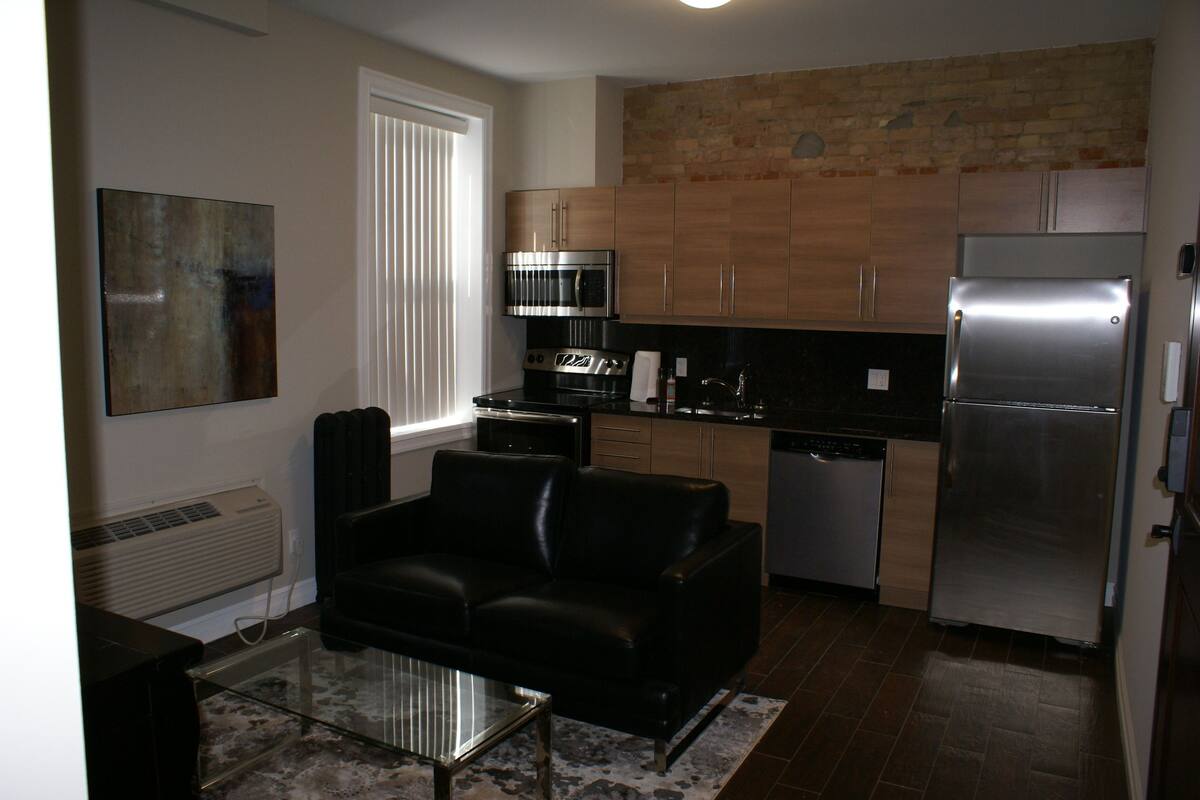 A modern kitchen with stainless steel appliances, a black leather sofa, and a glass coffee table.