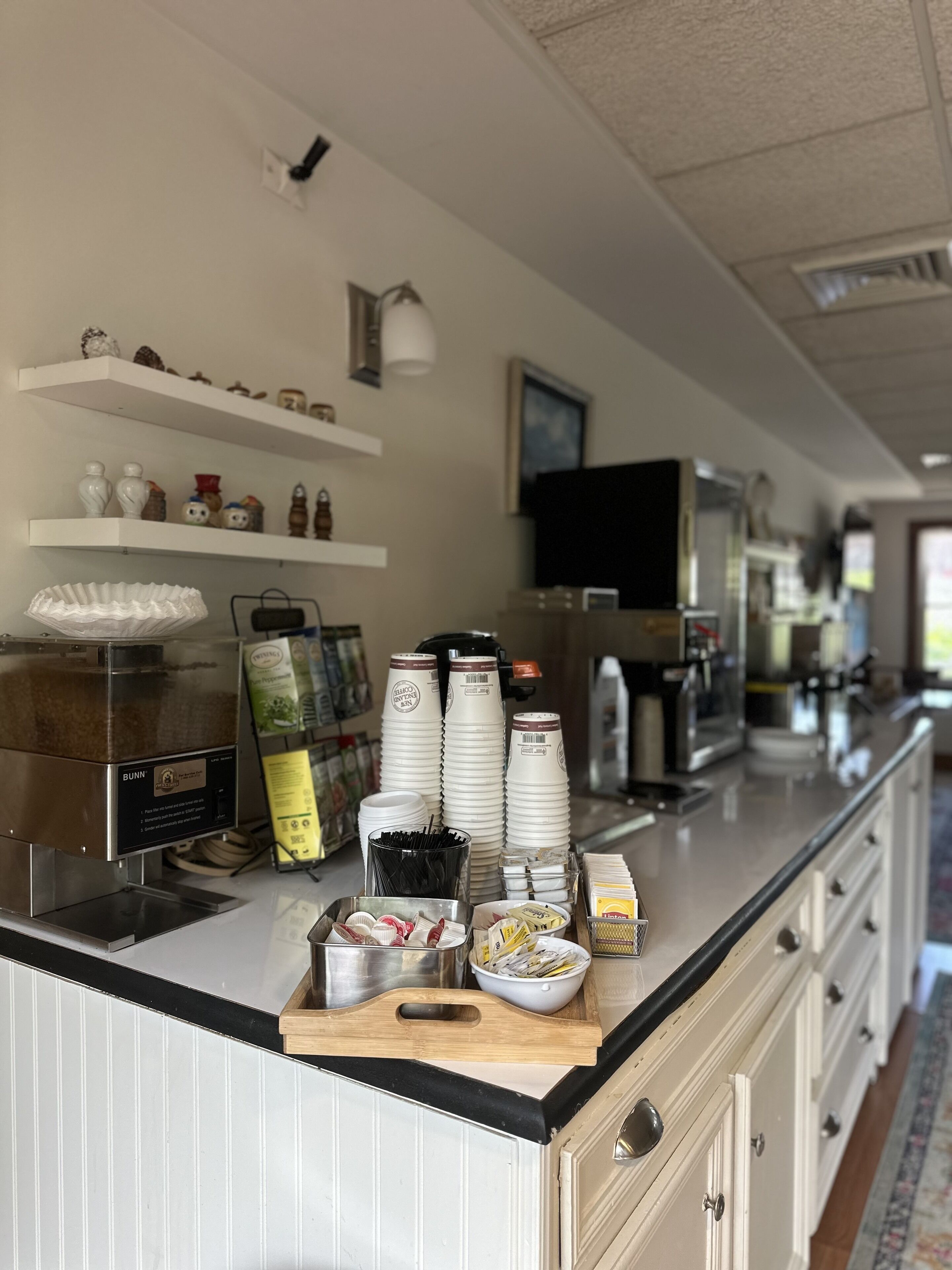 A kitchen area with a coffee machine, stacked paper cups, and various kitchen appliances.