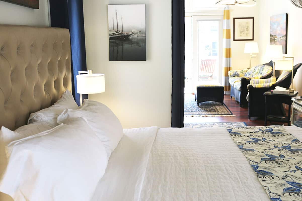 Quarto de hotel com uma cama grande, área de estar com sofá e poltronas, e vista para o exterior.