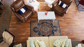 Una sala de estar con un sofá color beige, dos sillones de cuero marrón, una mesa de centro blanca y un tapete estampado.