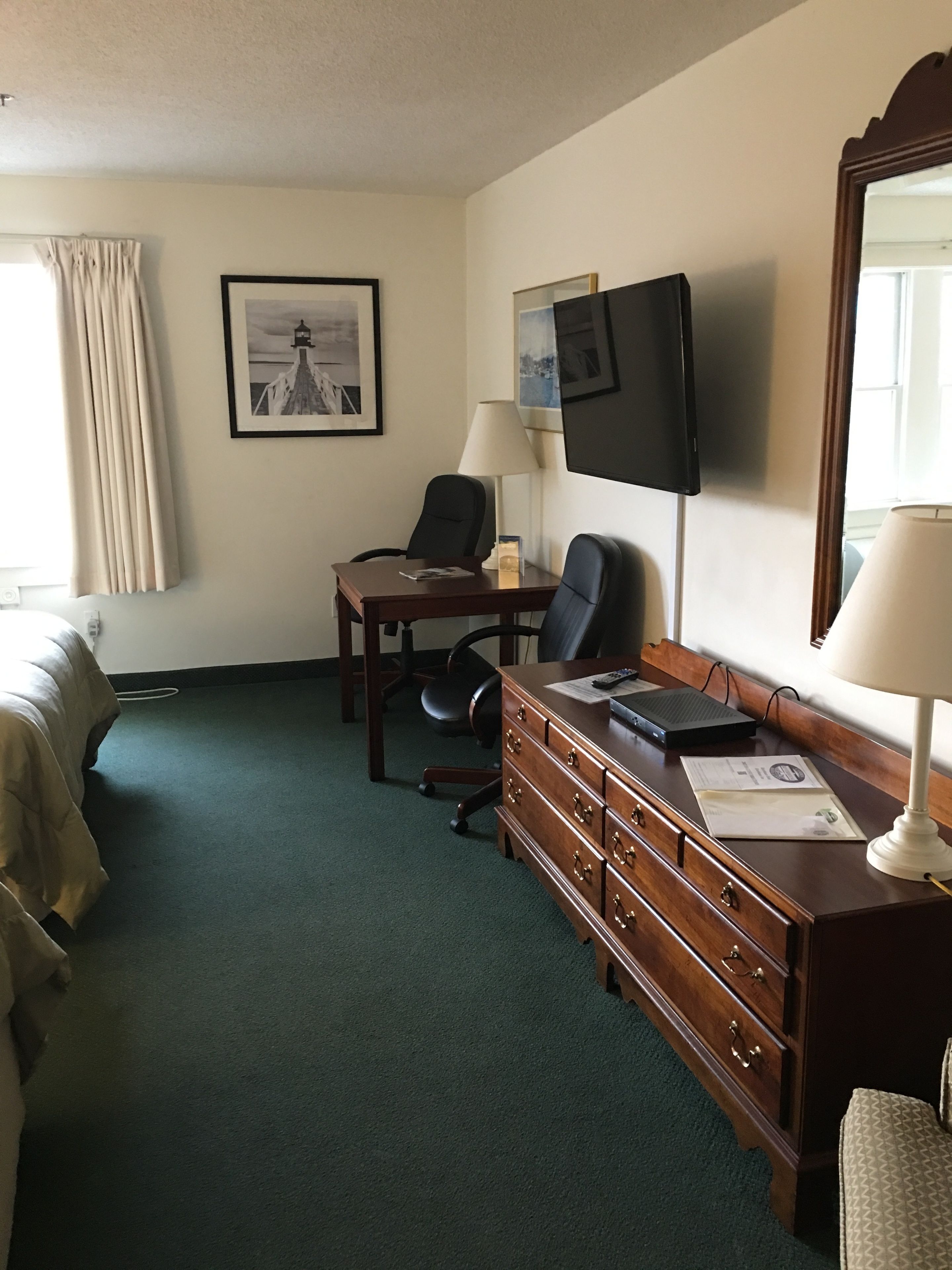 Habitación de hotel con cama, escritorio con silla, cómoda, televisor y ventana con cortinas.