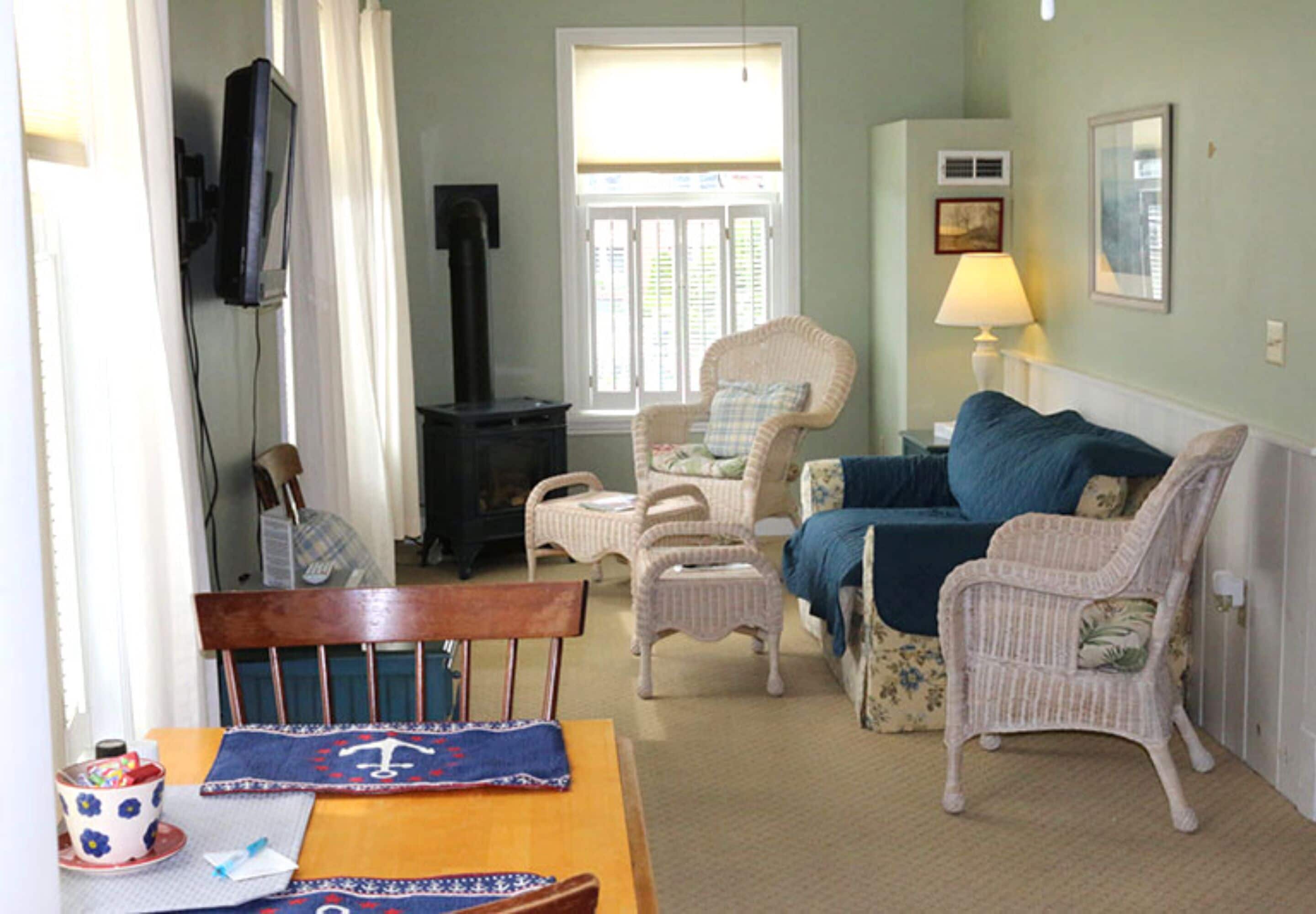 A cozy living room with a wooden table, wicker chairs, a blue sofa, and a television mounted on the wall.