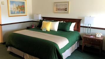 Een hotelkamer met een groot bed, beddengoed in groen en beige tinten, twee nachtkastjes met lampen, een bijzettafeltje met een klok en twee ingelijste foto's aan de muur.