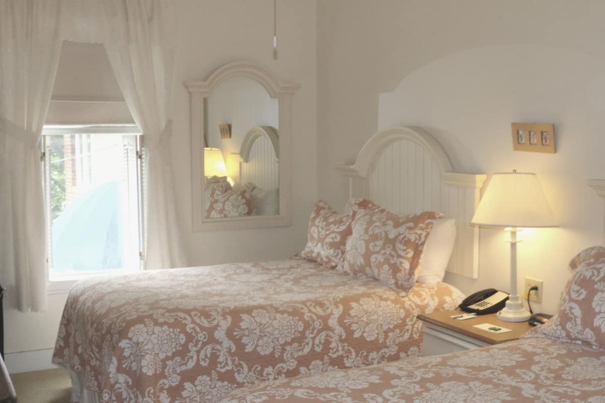 Quarto com duas camas, mesa de cabeceira com abajur, telefone e espelho.