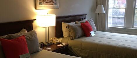 A hotel room with two beds, a nightstand with a telephone, a framed picture on the wall, and a window with curtains.