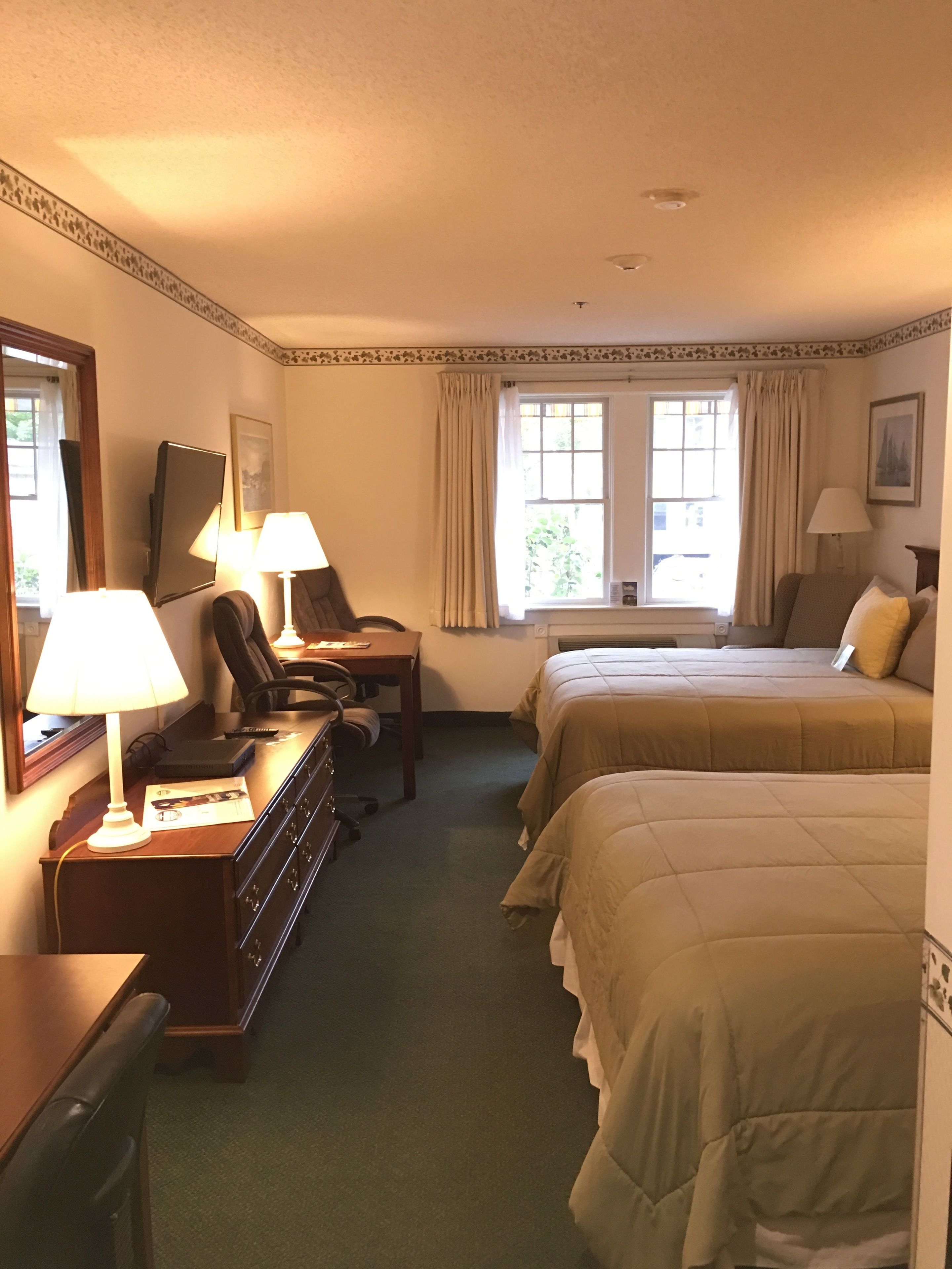 Una habitación de hotel con dos camas, un escritorio con lámpara, una silla y un aparador.