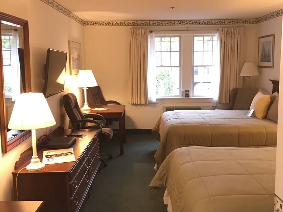 Una habitación de hotel con dos camas, un escritorio con lámpara, una silla y un aparador.
