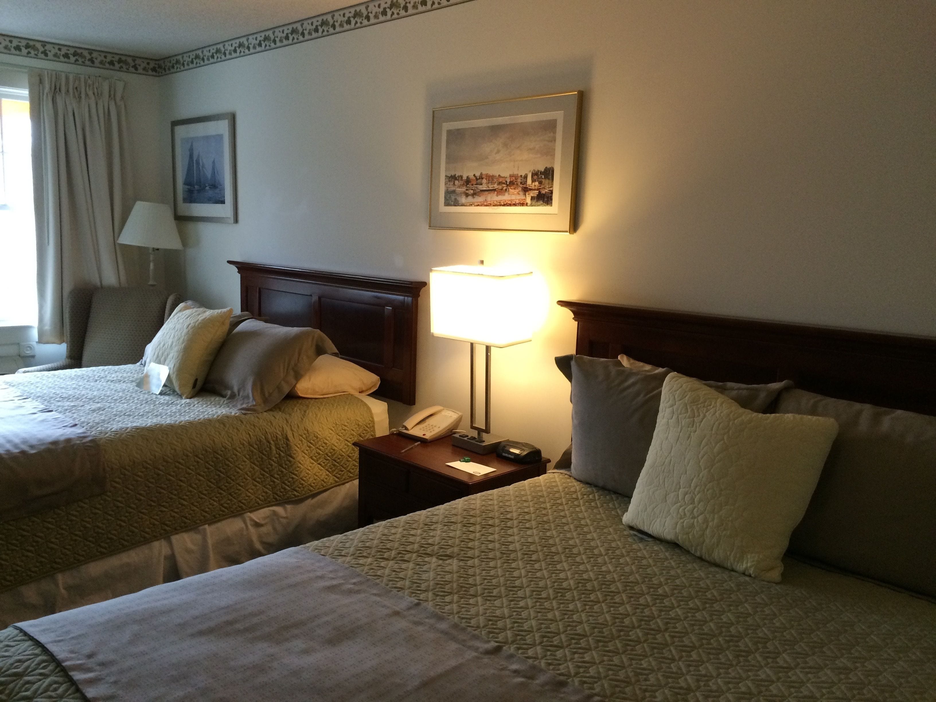 Une chambre d’hôtel avec deux lits, une table de chevet avec une lampe, un téléphone et un tableau encadré au mur.