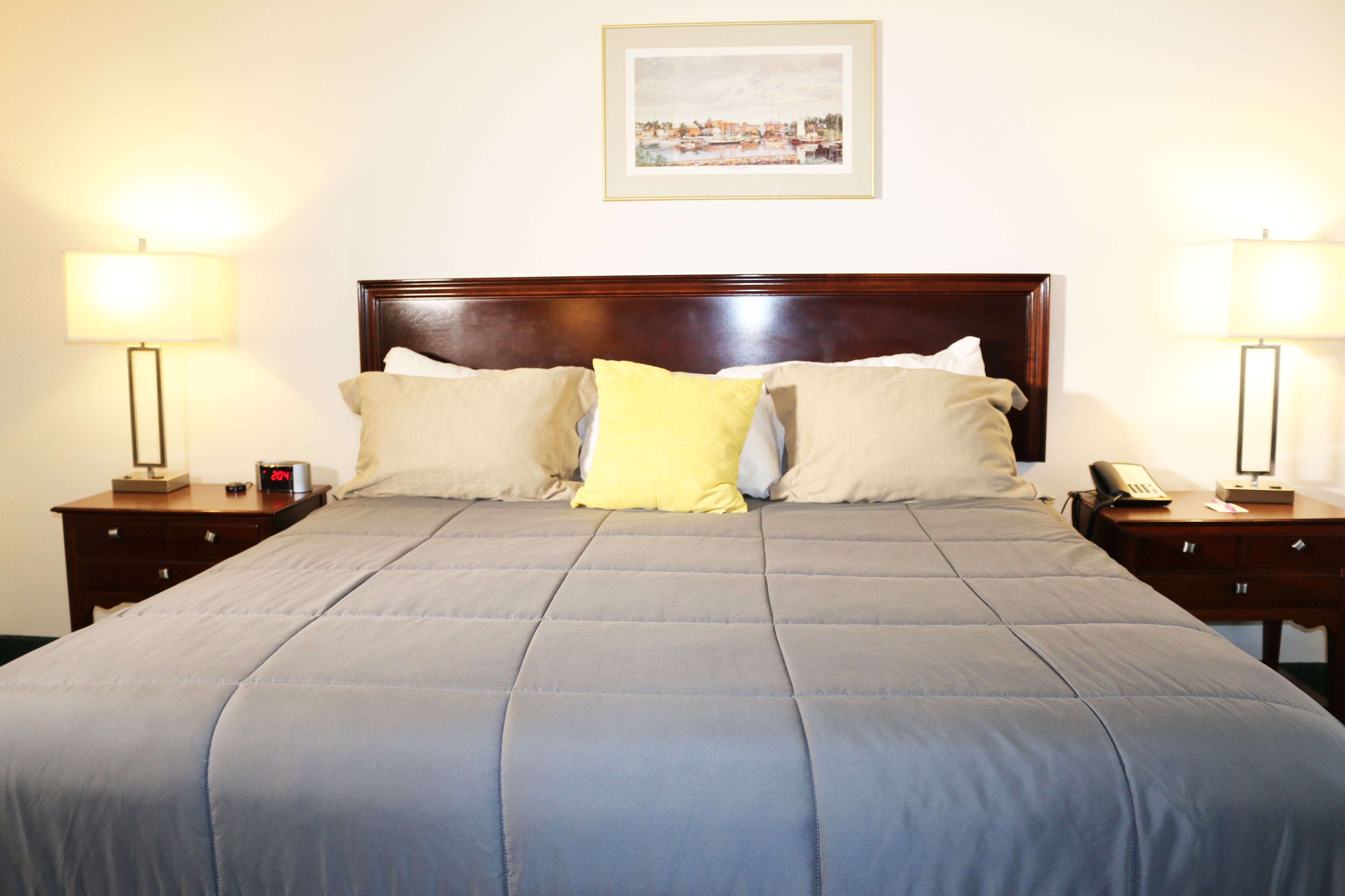 A neatly made bed with a grey duvet, two bedside tables with lamps, and a framed picture on the wall.
