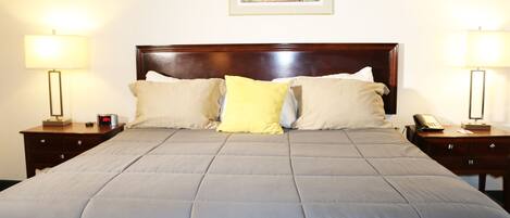 A neatly made bed with a grey duvet, two bedside tables with lamps, and a framed picture on the wall.