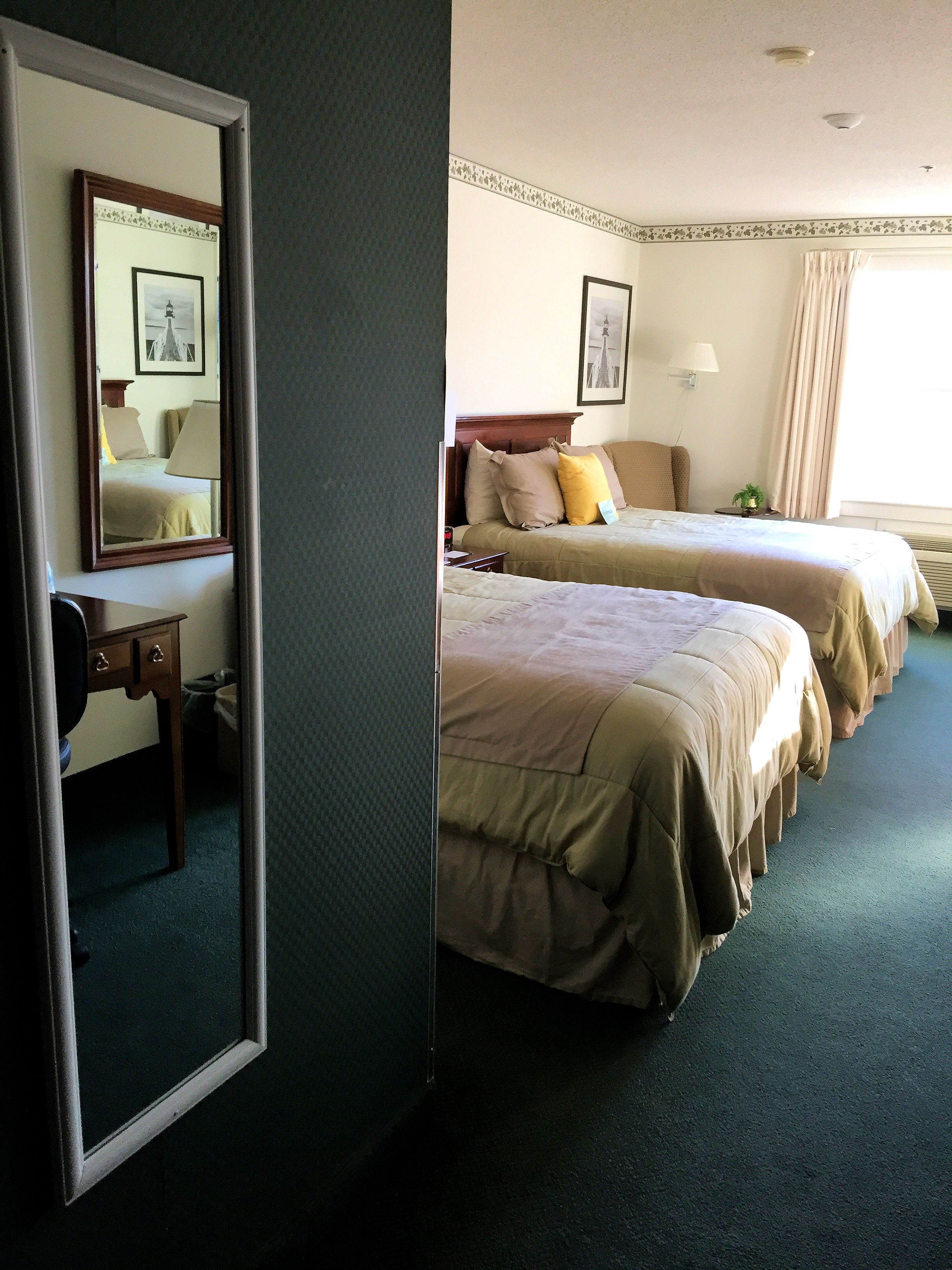 Una habitación de hotel con dos camas, un escritorio, un espejo y una ventana con cortinas.